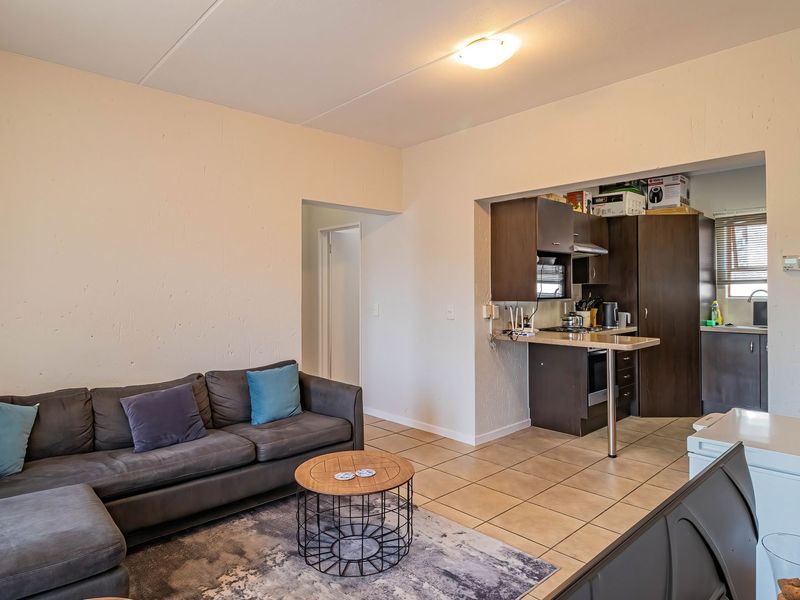 Open-plan living area featuring a functional kitchen with dark cabinetry, breakfast counter, and neutral tiled flooring throughout the space.