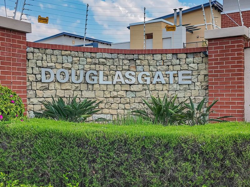 The entrance signage and boundary wall of the Douglasgate apartment complex, featuring stone cladding, brick pillars, and secure electric fencing.