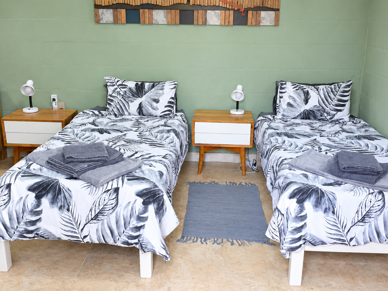 A bedroom featuring twin beds, tiled flooring, and painted exposed blockwork walls, providing a functional and simple sleeping space.