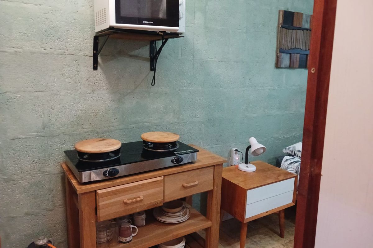 A compact kitchenette area featuring an exposed blockwork wall, wall-mounted microwave shelf, and a gas hob setup.
