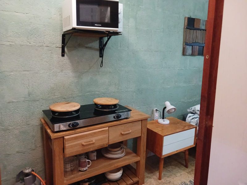 A compact kitchenette area featuring an exposed blockwork wall, wall-mounted microwave shelf, and a gas hob setup.