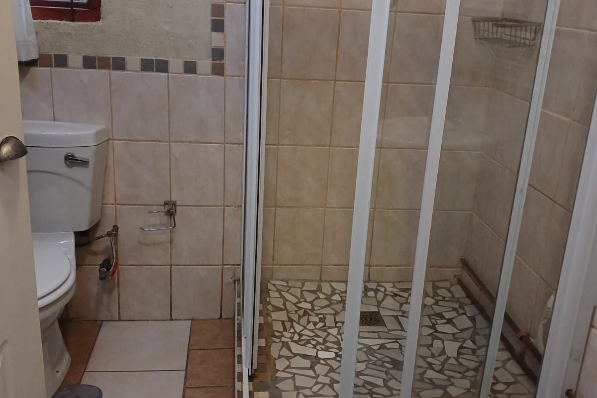 Compact bathroom featuring a shower enclosure with tiled base, standard toilet, and tiled wall finishes. Requires maintenance and cosmetic updates.