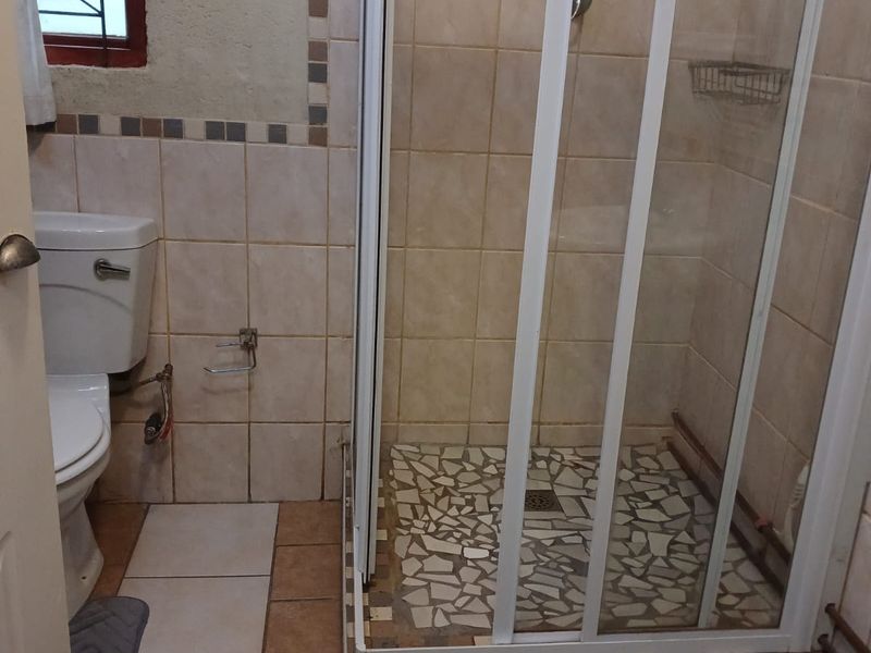 Compact bathroom featuring a shower enclosure with tiled base, standard toilet, and tiled wall finishes. Requires maintenance and cosmetic updates.