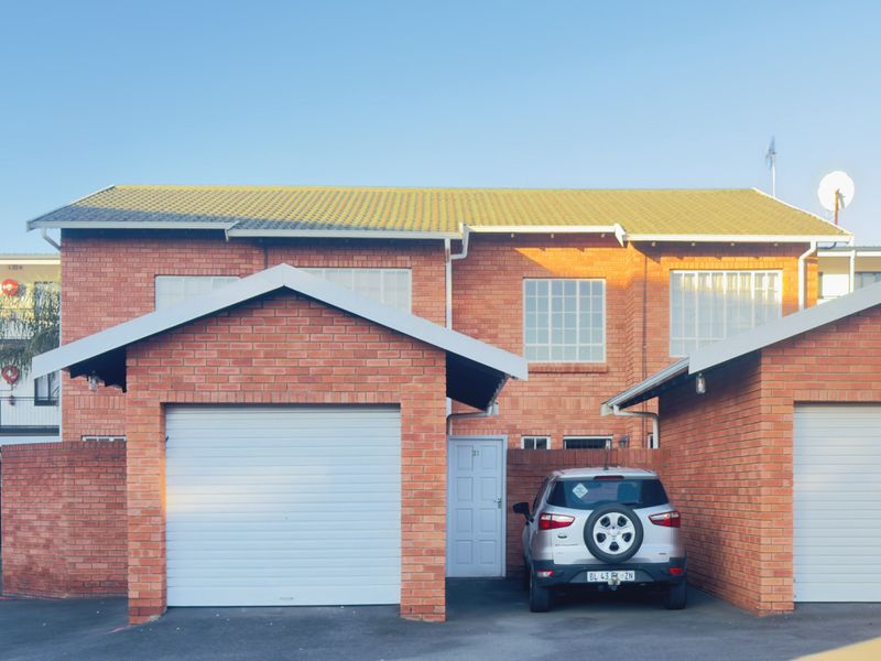 Front elevation of a face brick apartment unit featuring a garage and covered parking bay under a tiled roof.