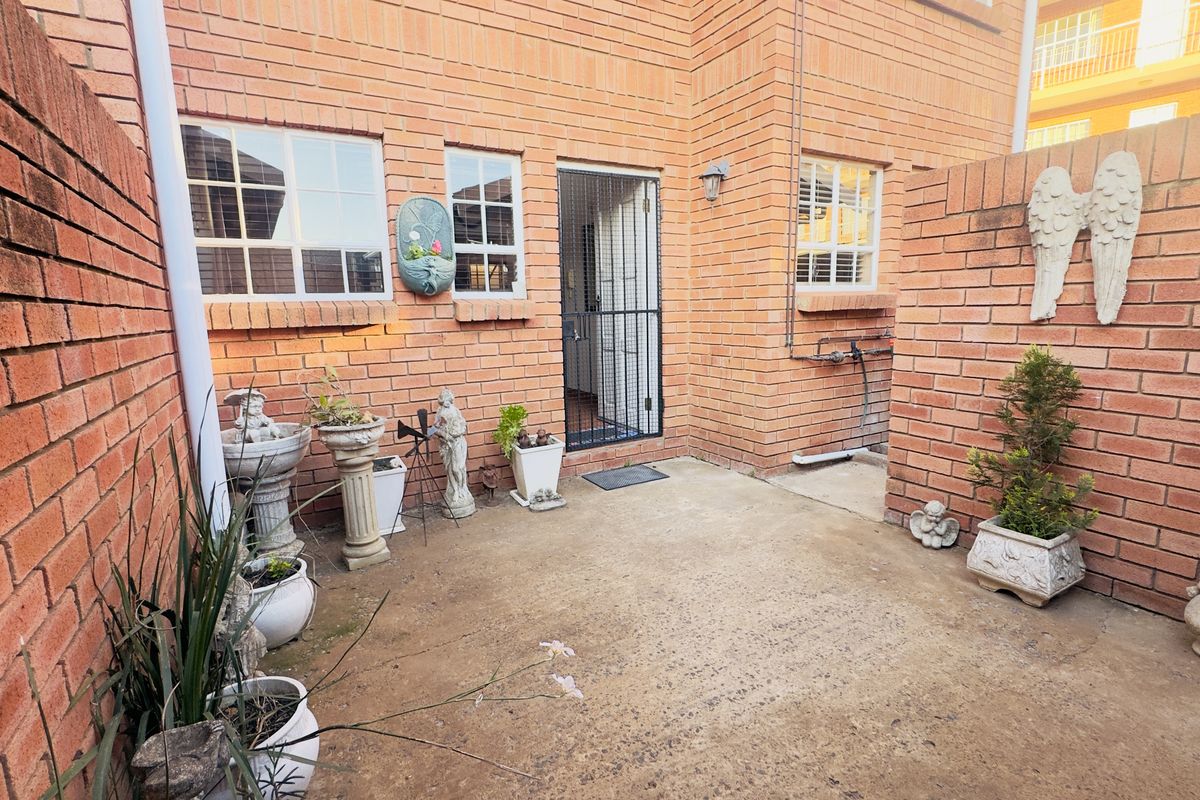 A private rear courtyard featuring exposed brick walls, a concrete patio area, and secure access to the apartment interior.