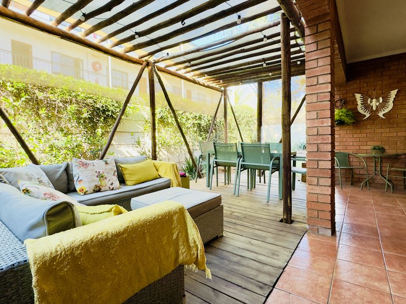 A covered outdoor patio area featuring a timber pergola, brick pillar accents, and a combination of tiled and timber decking surfaces.