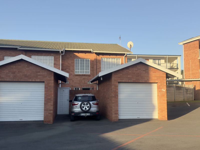 Front exterior view of the apartment complex featuring two brick-built single garages with roller shutter doors and a paved driveway area.