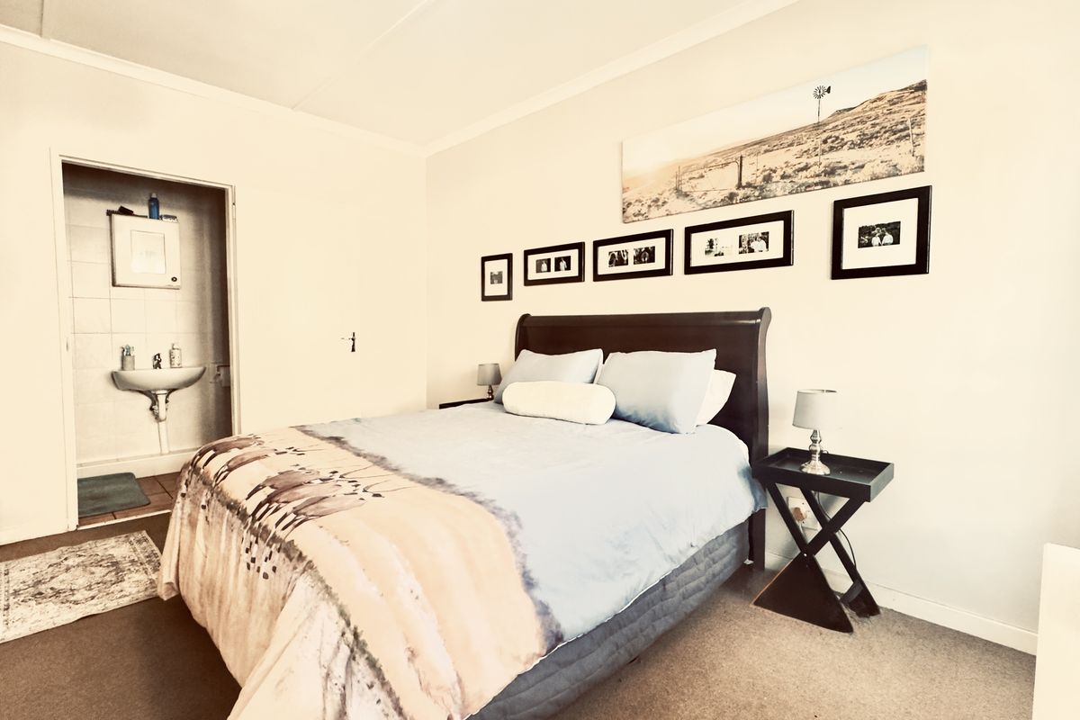 A comfortable bedroom featuring neutral walls, carpeted flooring, and an attached en-suite bathroom with a wall-mounted basin.
