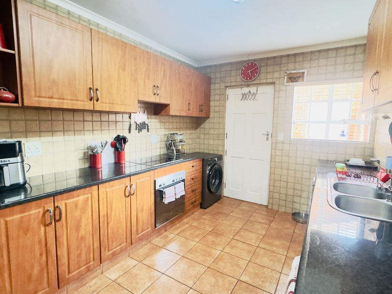 A functional kitchen featuring wood-look cabinetry, granite countertops, a double bowl sink, and integrated laundry plumbing, finished with tiled walls and floors.