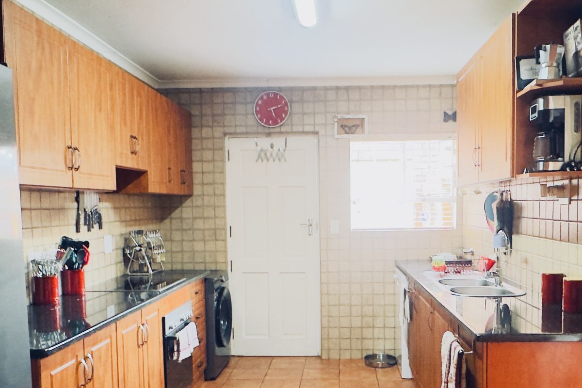 A functional galley-style kitchen featuring wooden cabinetry, granite countertops, integrated oven, and tiled finishes throughout.