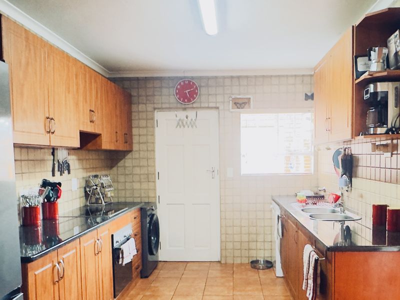 A functional galley-style kitchen featuring wooden cabinetry, granite countertops, integrated oven, and tiled finishes throughout.