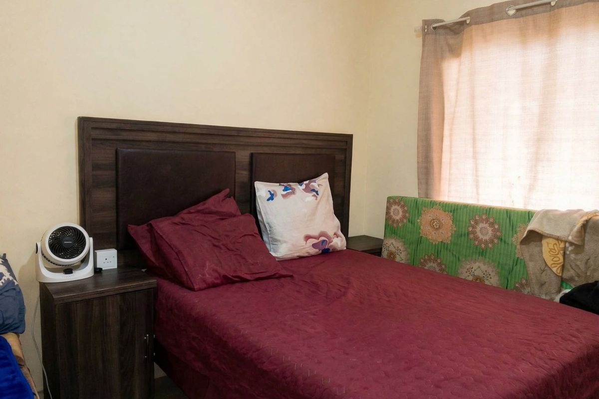 A functional bedroom space featuring a neutral wall finish and a window with a curtain rod.