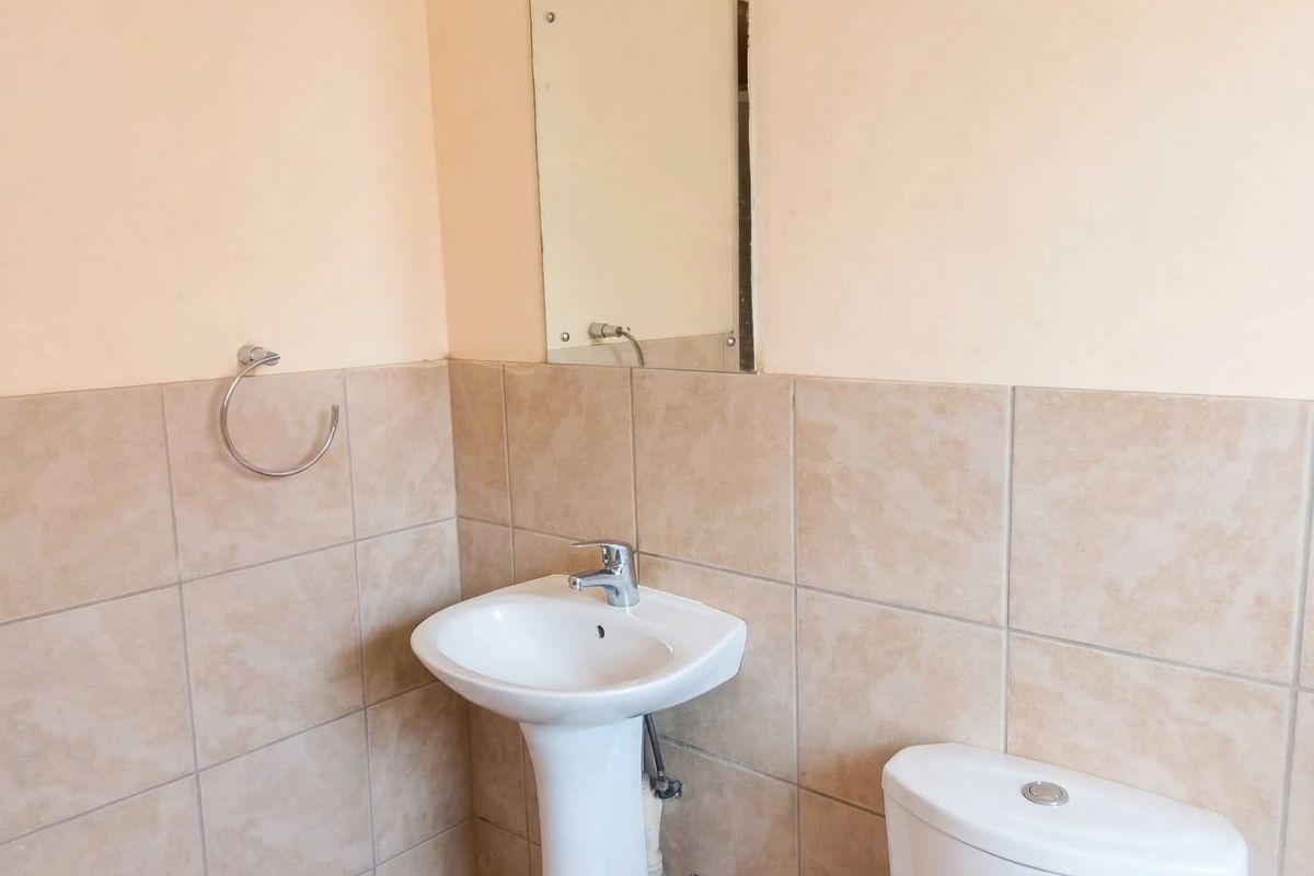 A functional bathroom featuring a pedestal basin with a chrome mixer tap, a wall-mounted mirror, and neutral ceramic wall tiling.
