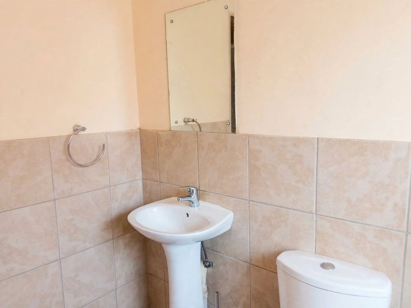 A functional bathroom featuring a pedestal basin with a chrome mixer tap, a wall-mounted mirror, and neutral ceramic wall tiling.