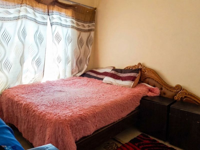 A bedroom featuring a carved wooden headboard and window curtains.
