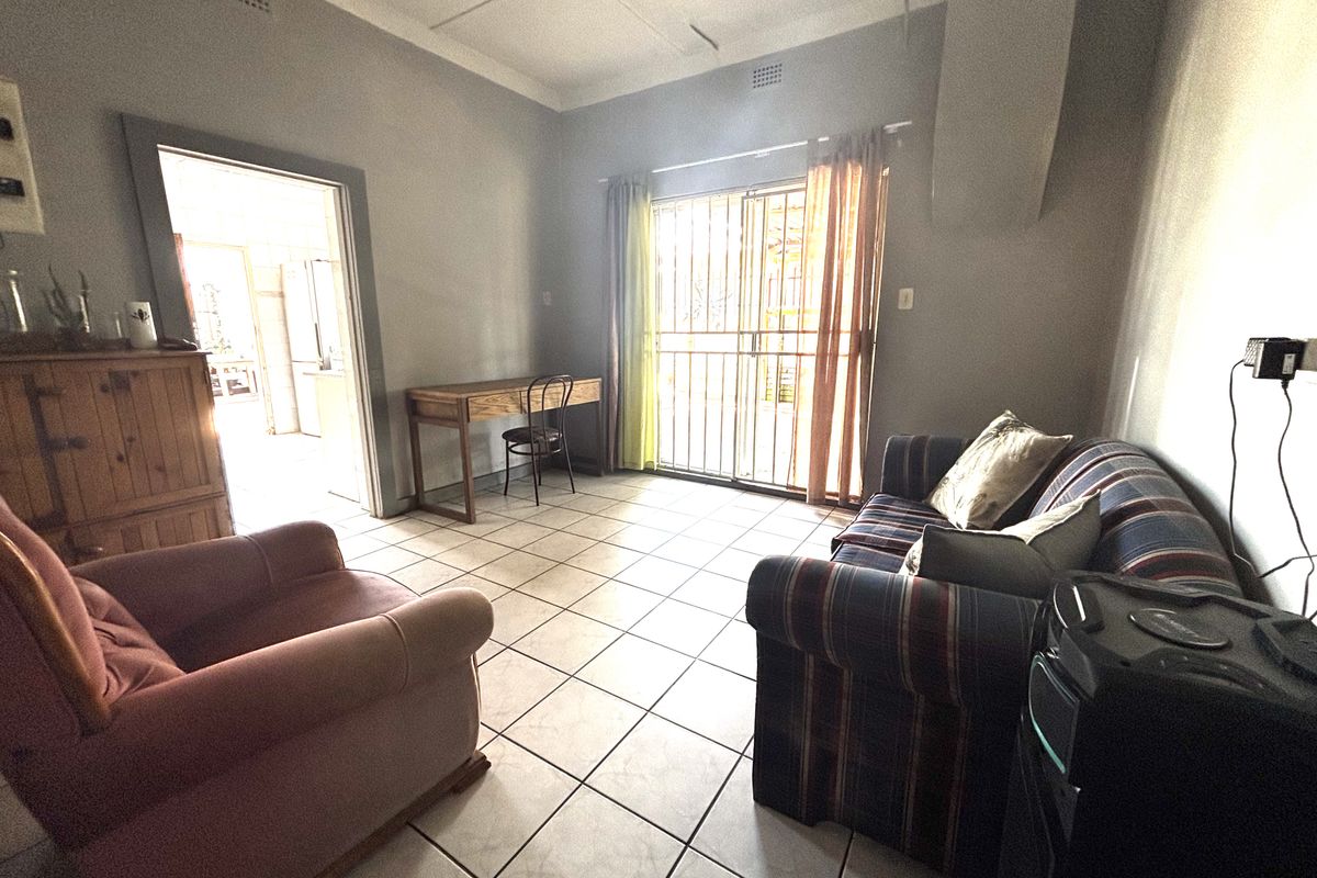 A living room featuring tiled flooring and a sliding glass door with security gate, providing access to the exterior.