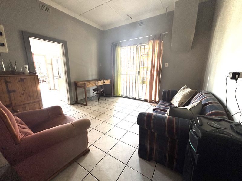 A living room featuring tiled flooring and a sliding glass door with security gate, providing access to the exterior.