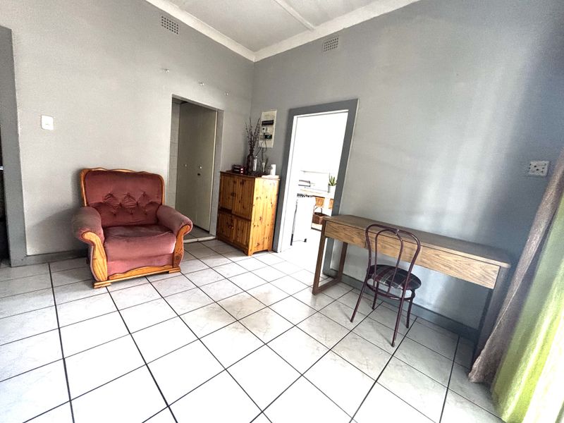 A living area featuring tiled flooring and coved ceilings, providing a functional space with access to adjacent rooms.
