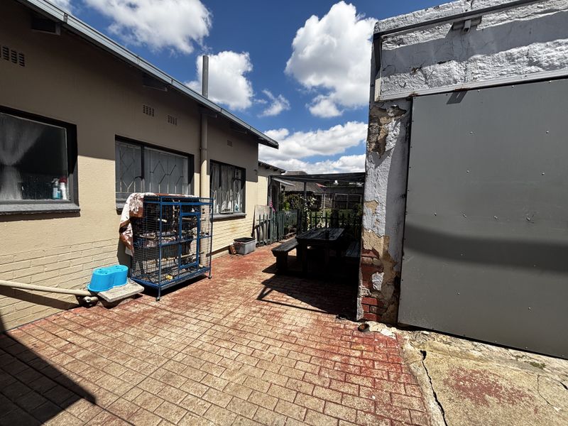 Rear exterior area featuring a paved patio space between the main house and a garage structure, showing signs of wear on the exterior walls.