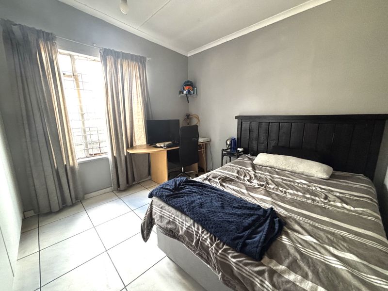 A functional bedroom featuring tiled flooring, a window with security bars, and neutral wall finishes.