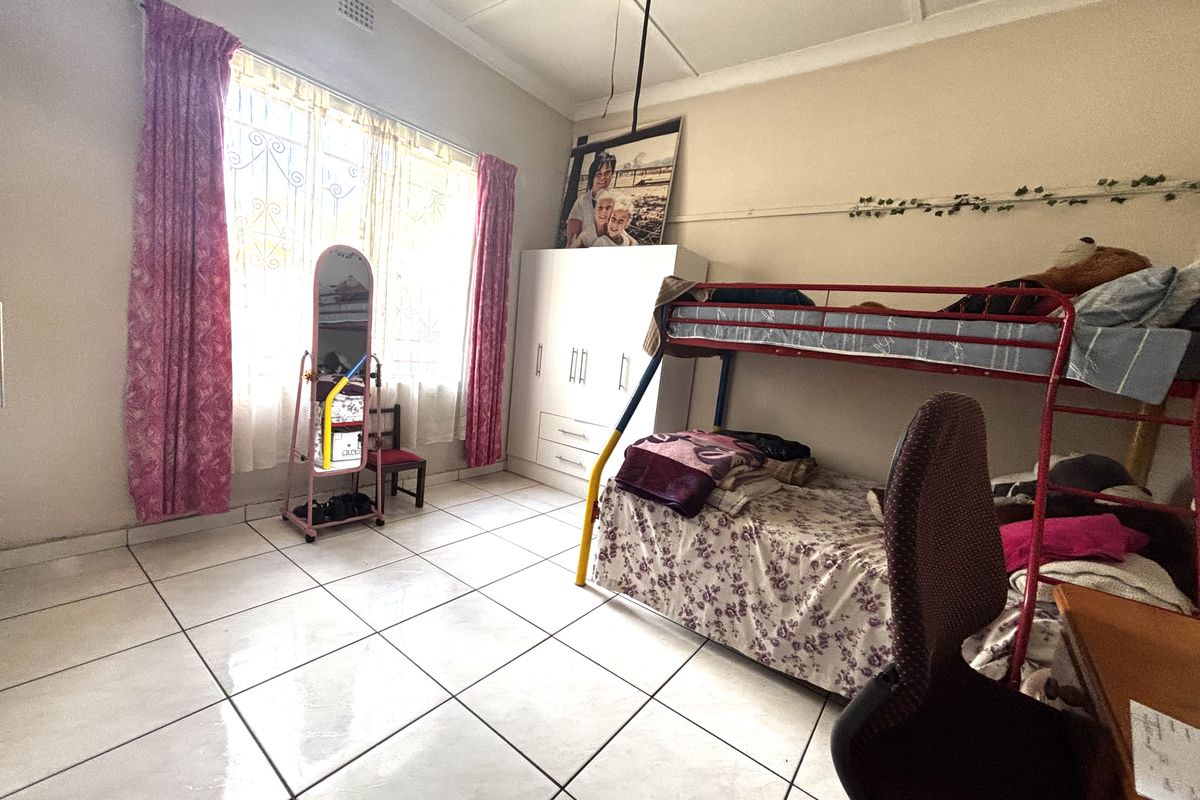 A bedroom featuring tiled flooring, a ceiling fan, and a built-in wardrobe, with security bars installed on the window.