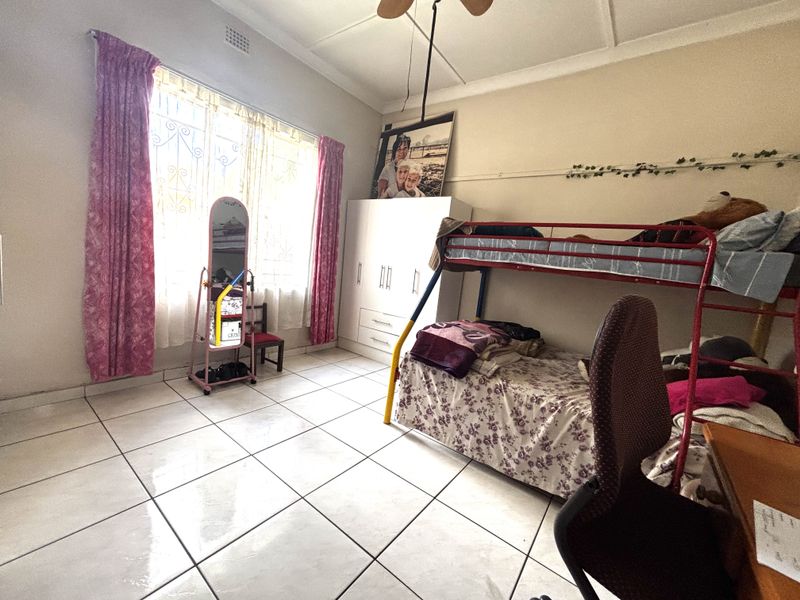 A bedroom featuring tiled flooring, a ceiling fan, and a built-in wardrobe, with security bars installed on the window.