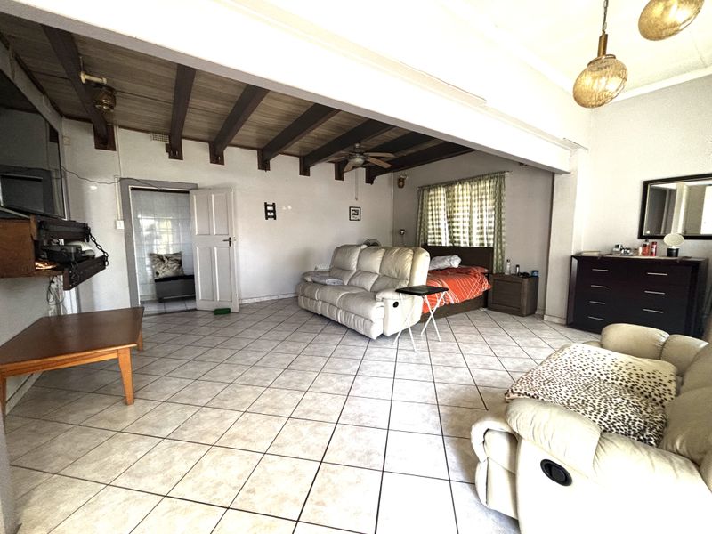 Spacious open-plan living area featuring exposed timber ceiling beams, ceramic tiled flooring, and a ceiling fan, offering a versatile layout for living and sleeping.