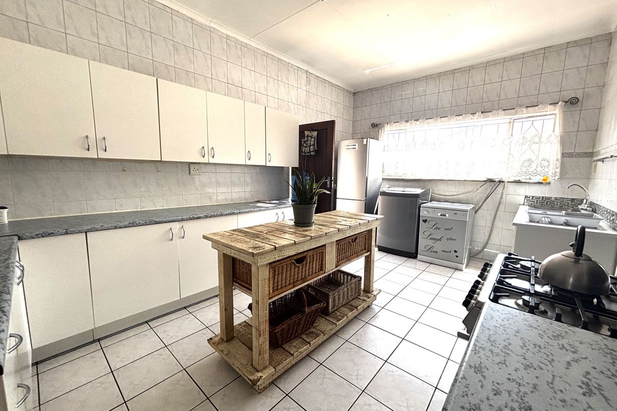 A functional kitchen featuring white cabinetry, laminate countertops, a gas hob, and tiled finishes, offering a practical layout for daily meal preparation.