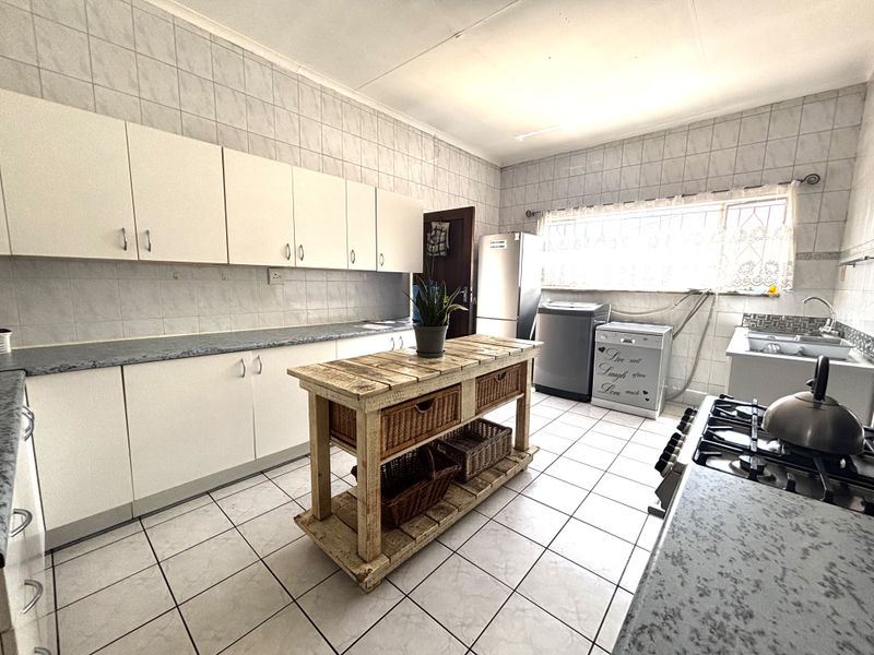 A functional kitchen featuring white cabinetry, laminate countertops, a gas hob, and tiled finishes, offering a practical layout for daily meal preparation.