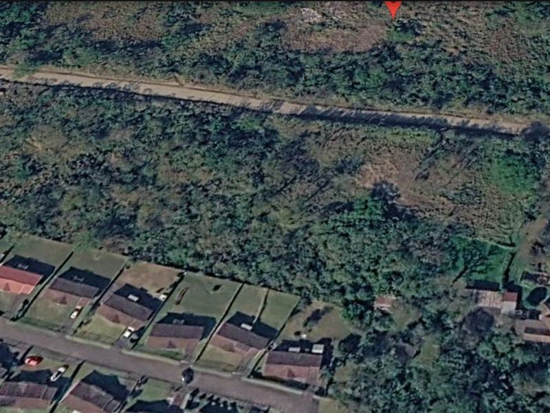 An aerial view of a vacant residential plot featuring natural vegetation, situated in a developed neighborhood.