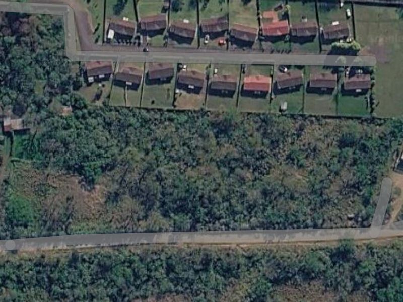 Aerial view of a vacant residential land plot featuring dense vegetation and proximity to local road infrastructure.