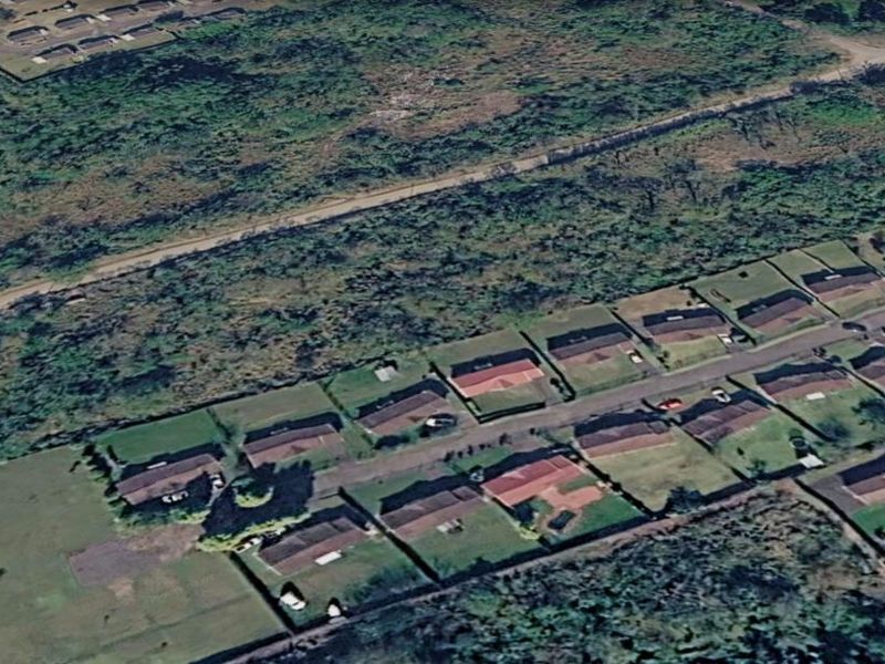 An aerial view of a residential neighborhood showing multiple plots, paved streets, and surrounding natural landscape.
