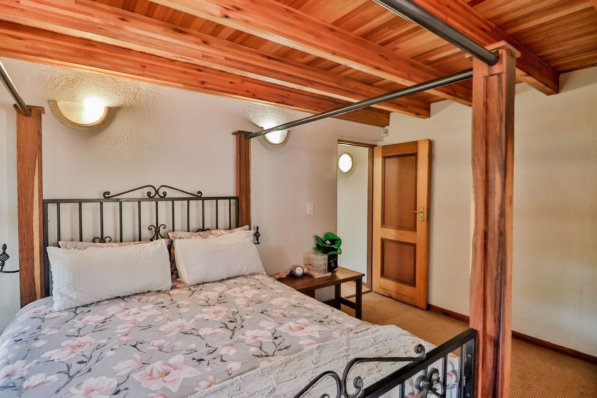 A bedroom featuring a distinctive exposed timber beam ceiling, wall-mounted sconce lighting, and a solid wood door leading to an adjacent space.
