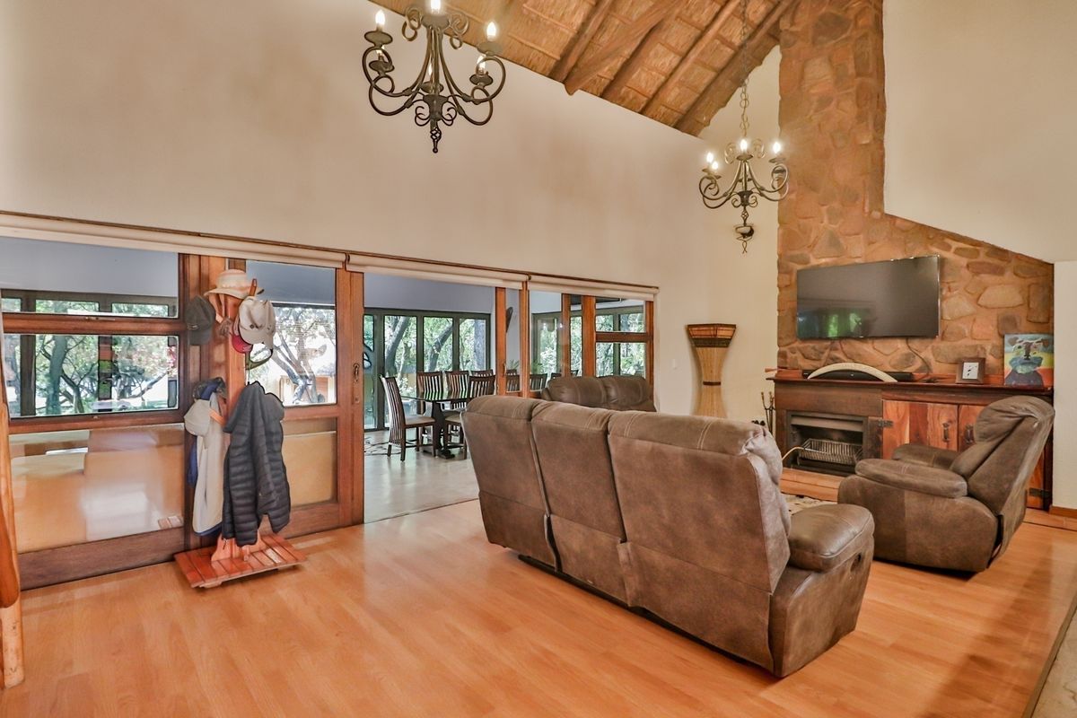 Spacious living room featuring a vaulted timber ceiling, stone-clad fireplace, and large sliding glass doors opening to an adjacent dining area.