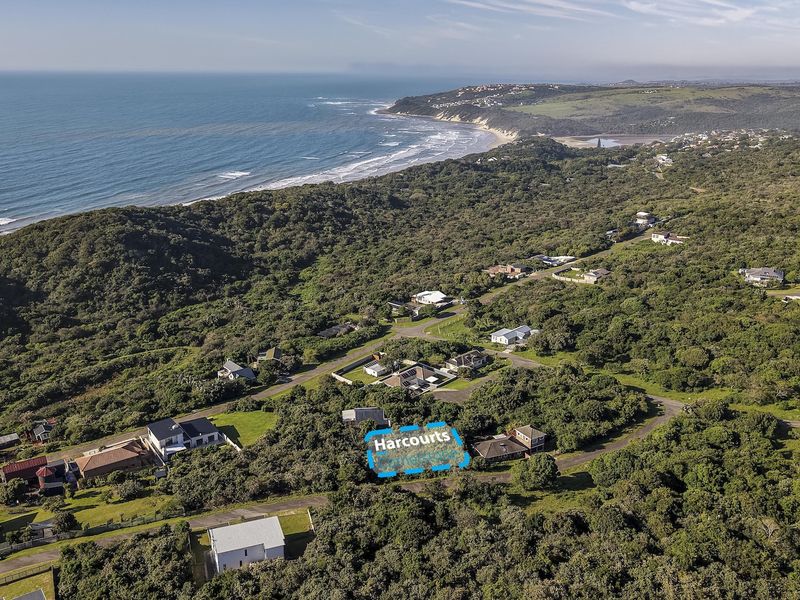 An aerial view of a vacant residential plot situated within a coastal landscape, surrounded by lush vegetation and established residential properties.