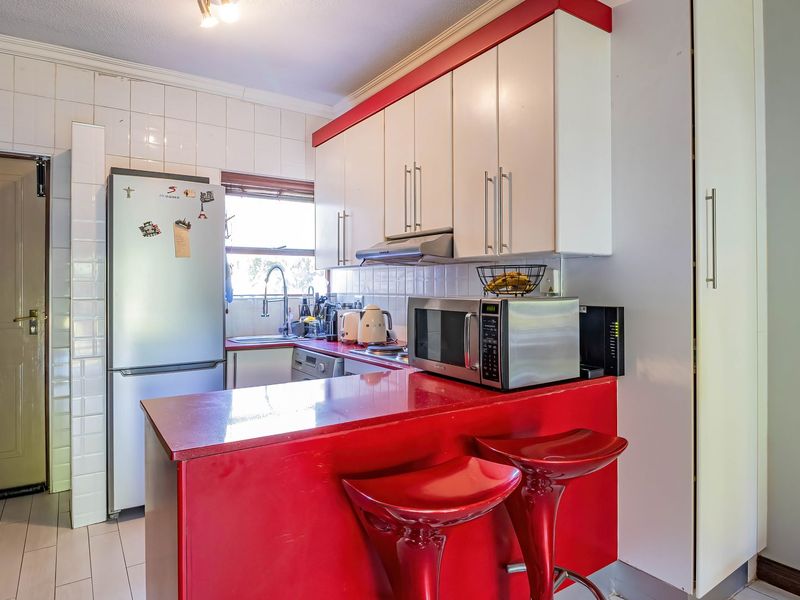 A compact kitchen featuring white upper cabinetry, a vibrant red breakfast bar, tiled backsplash, and integrated sink area.