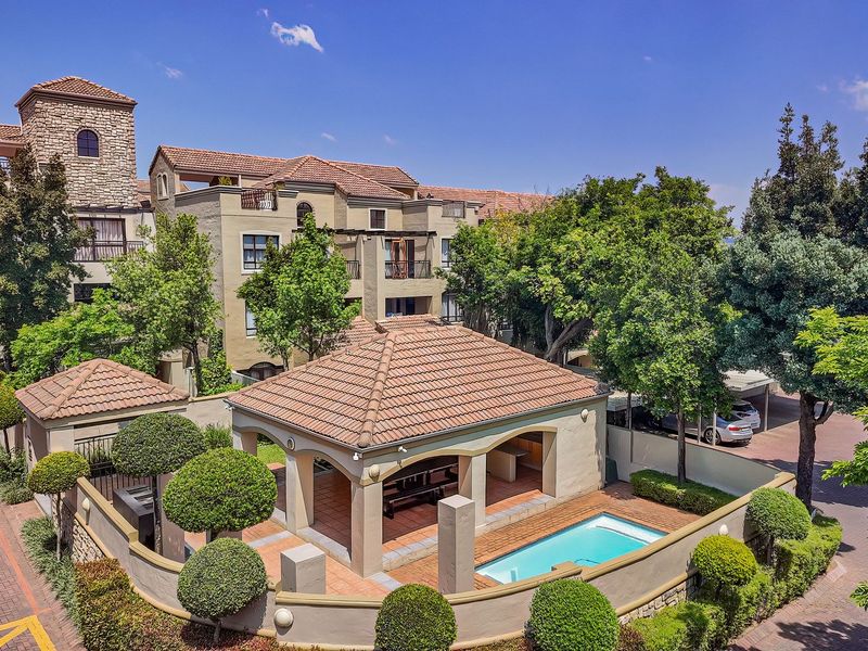 An elevated view of a residential apartment complex featuring a communal swimming pool, covered patio area, and well-maintained landscaped gardens.