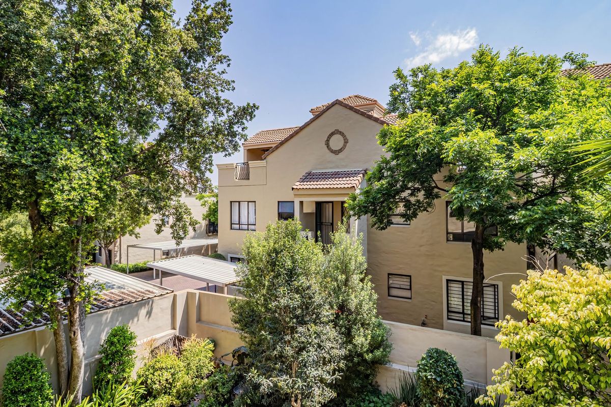 A view of the rear exterior of the apartment complex, featuring a stucco facade, tiled roof, and a covered carport area.