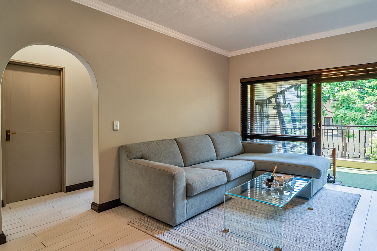 A bright living room featuring tiled flooring, an elegant archway, and a large sliding glass door providing access to a private balcony.