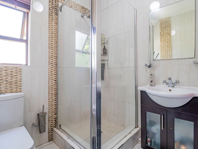 A functional bathroom featuring a glass shower enclosure, a vanity unit with a basin, and neutral wall tiling.