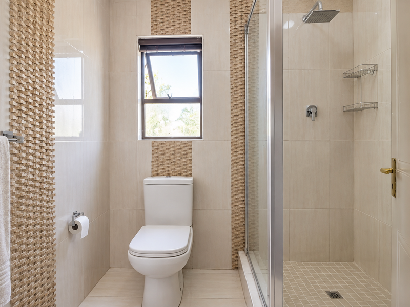 A well-maintained bathroom featuring a glass-enclosed shower, modern toilet, and neutral tiled finishes with decorative textured wall accents.