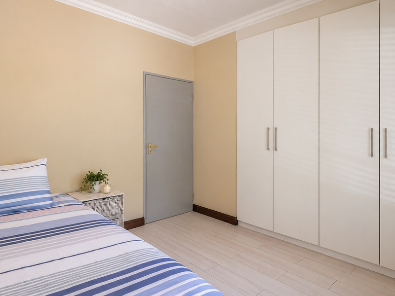 A well-maintained bedroom featuring light laminate flooring, neutral wall tones, and ample built-in cupboard storage with modern finishes.