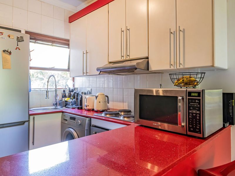 A compact kitchen featuring red stone countertops, white cabinetry, tiled backsplash, and integrated appliances including a washing machine and extractor fan.