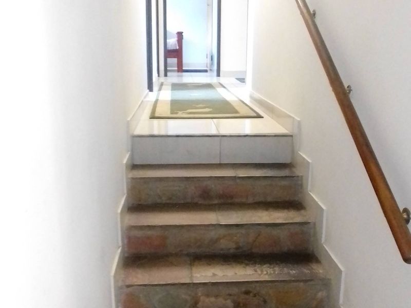 A narrow interior hallway featuring a stone staircase with a wooden handrail leading to a tiled landing area.