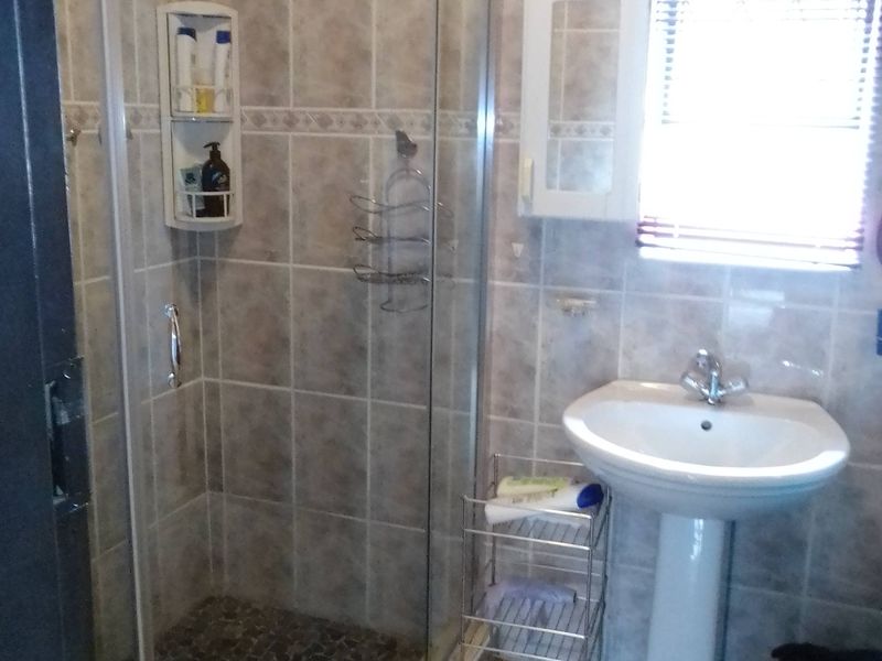 A functional bathroom featuring a corner shower enclosure, pedestal basin, and neutral wall tiling with a window for natural light.