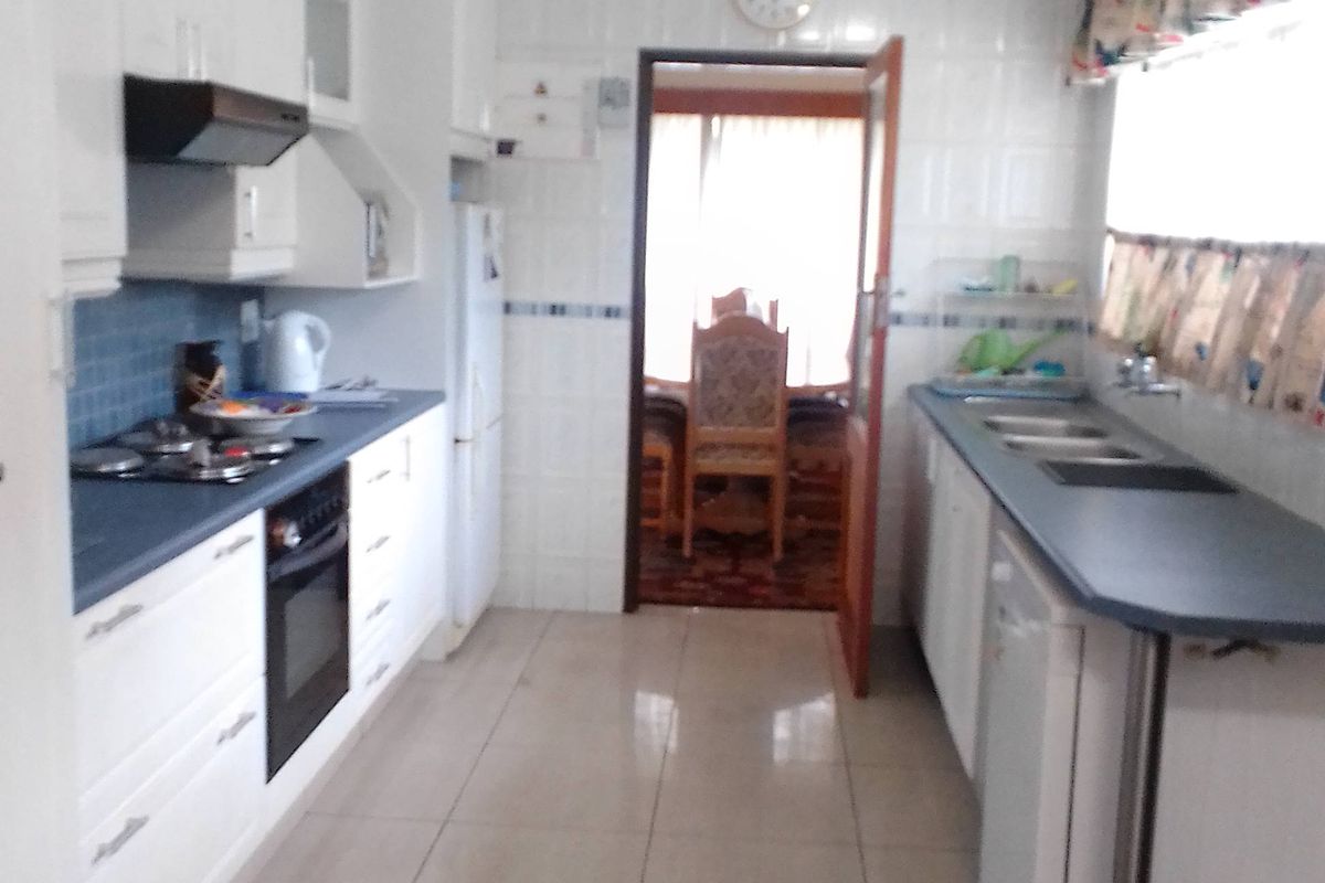 A functional galley-style kitchen featuring white cabinetry, a gas hob, built-in oven, and tiled finishes throughout.