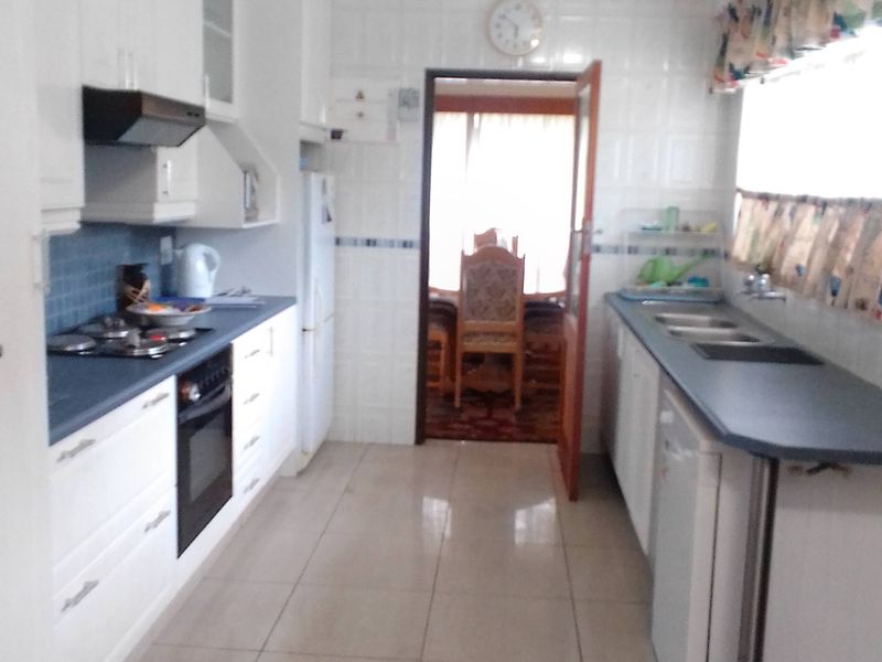 A functional galley-style kitchen featuring white cabinetry, a gas hob, built-in oven, and tiled finishes throughout.