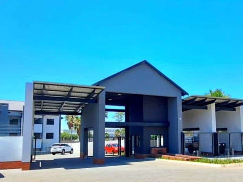 Modern apartment complex entrance featuring a secure gated access point, guard house, and covered parking bays with a contemporary architectural design.