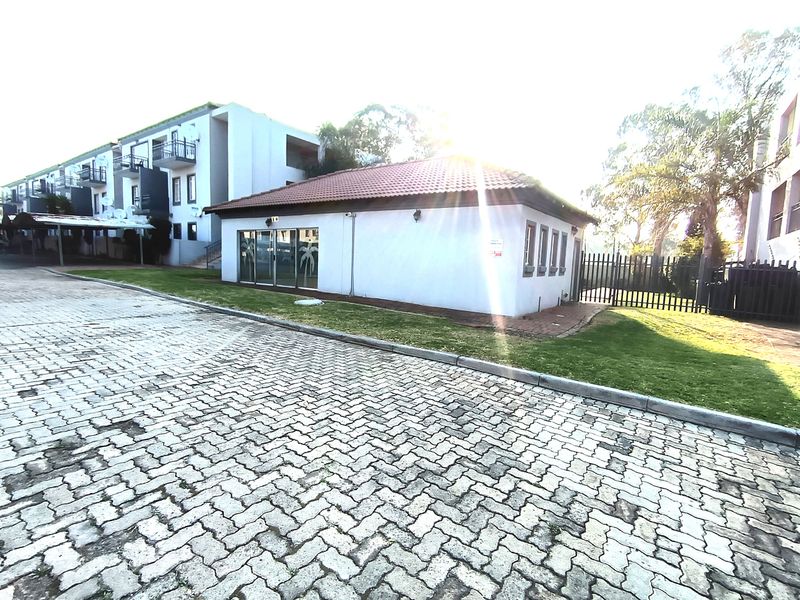 Exterior view of the apartment complex featuring a paved driveway, a standalone building with a tiled roof, and secure perimeter fencing.