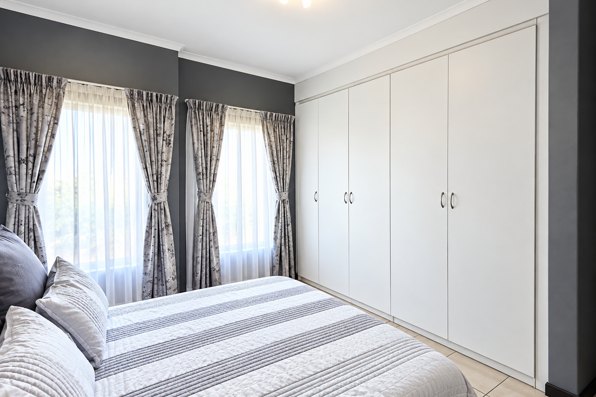 A well-maintained bedroom featuring neutral tiled flooring, dark accent walls, and extensive floor-to-ceiling built-in cupboards providing ample storage space.